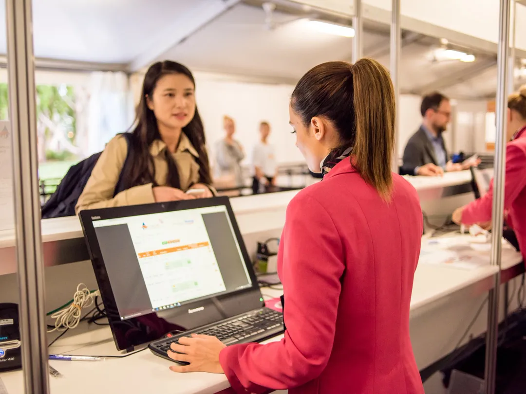 Event staff working on laptops at a registration desk while a delegate checks in